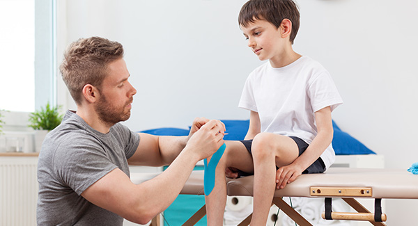 man bandaging boy's knee