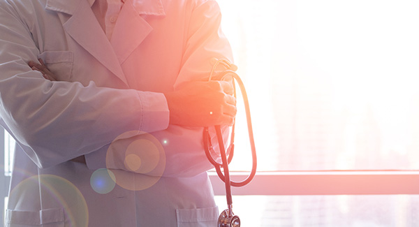 Body of doctor with arms crossed and sun behind him.