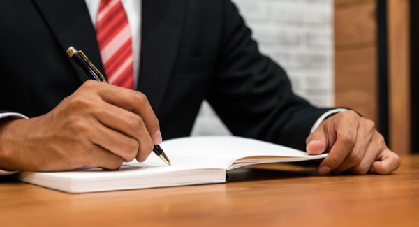 Man in red tie writing in notebook